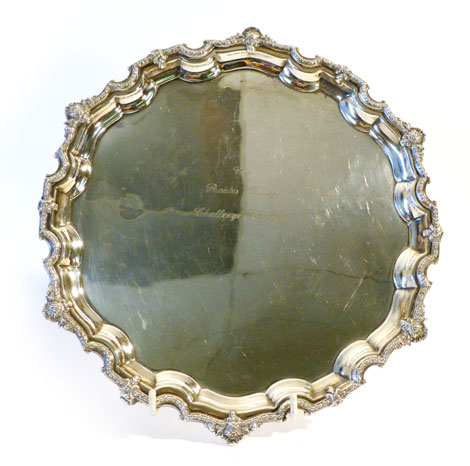 A silver salver with pie crust edge decorated with a flower head border interspersed with shield