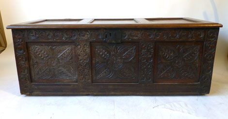 An 18th century three panelled coffer with a panelled top above a carved face with foliate and