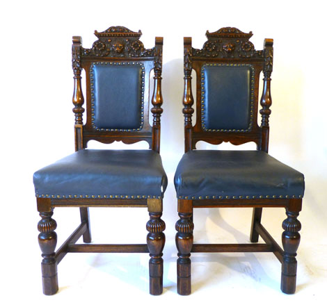 A pair of carved oak dining chairs, the back rest with lion head and floral motifs on baluster