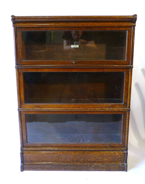 A Globe Wernicke oak three tier book case with glazed shelves on a plinth base, ivorine label,