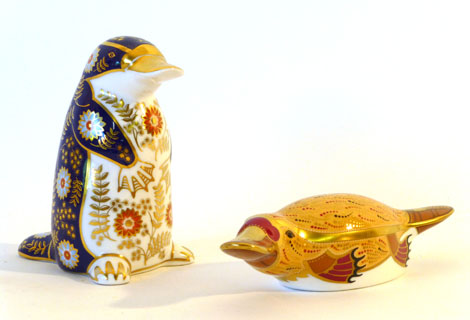 A Royal Crown Derby paperweight of a duck-billed platypus with gold button together with another