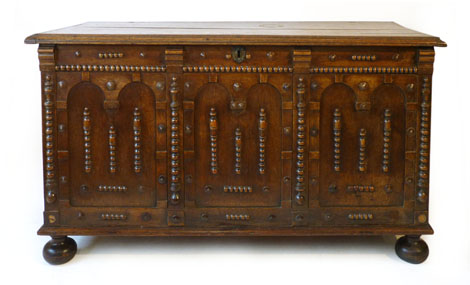 An 18th century style oak coffer with plank top over a three panelled top with moulded motifs on bun