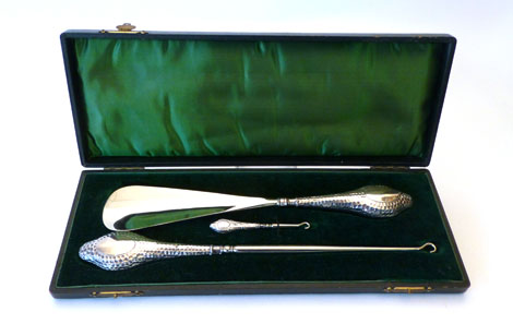 A cased set of Edwardian silver handled button hooks and a shoe horn with a hammered finish, maker