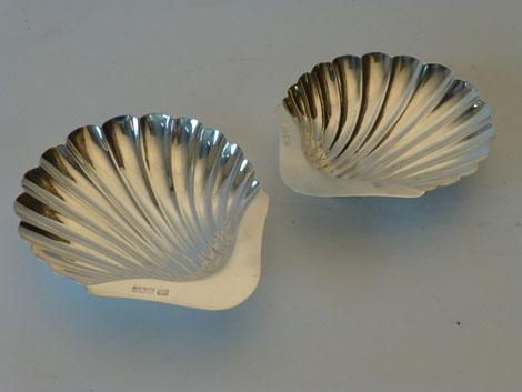 A pair of Edwardian silver scalloped shaped butter dishes with plain thumb pieces, each raised on