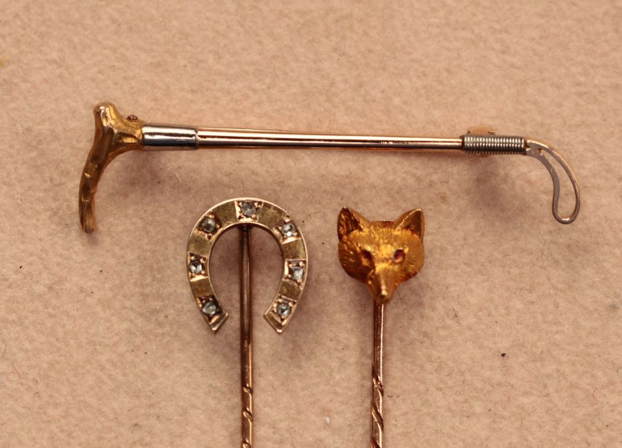 A group of three gold stick pins modelled as a fox, a riding crop and diamond set horseshoe,