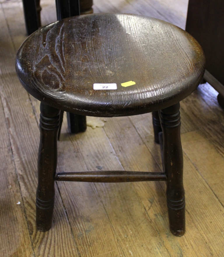 An early 20th century oak staid stool with dished seat, raised on turned legs with stretcher