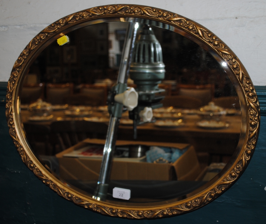 An oval shaped wall mirror with bevelled glass with an ornate gilt frame