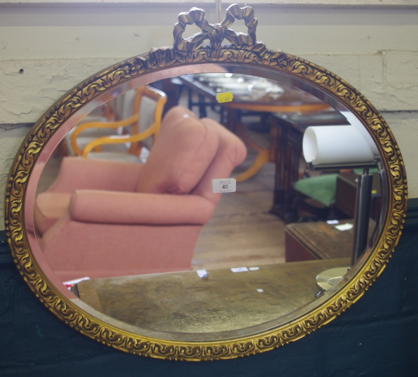 An oval shaped wall mirror with bevelled glass surrounded by an elaborately carved gilt frame