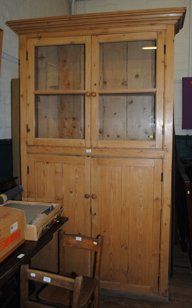 A 19th century pine kitchen storage press with shaped corners with two glazed doors with turned
