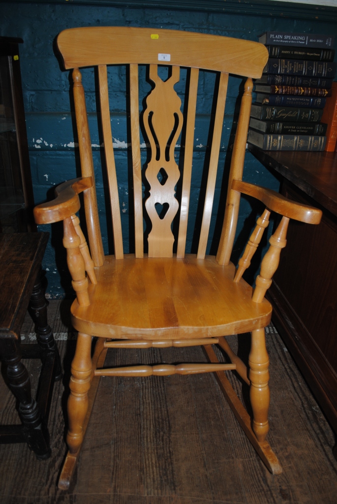 A Windsor style beech rocking chair with shaped splat, curved arms, supported on turned legs and