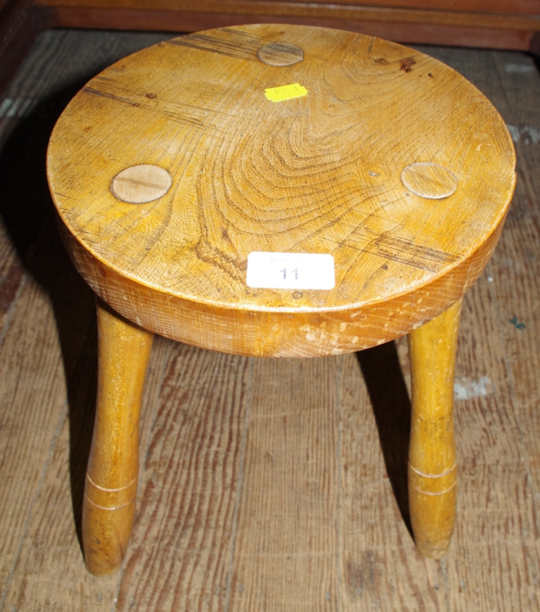 A three legged circular milking stool with an elm seat