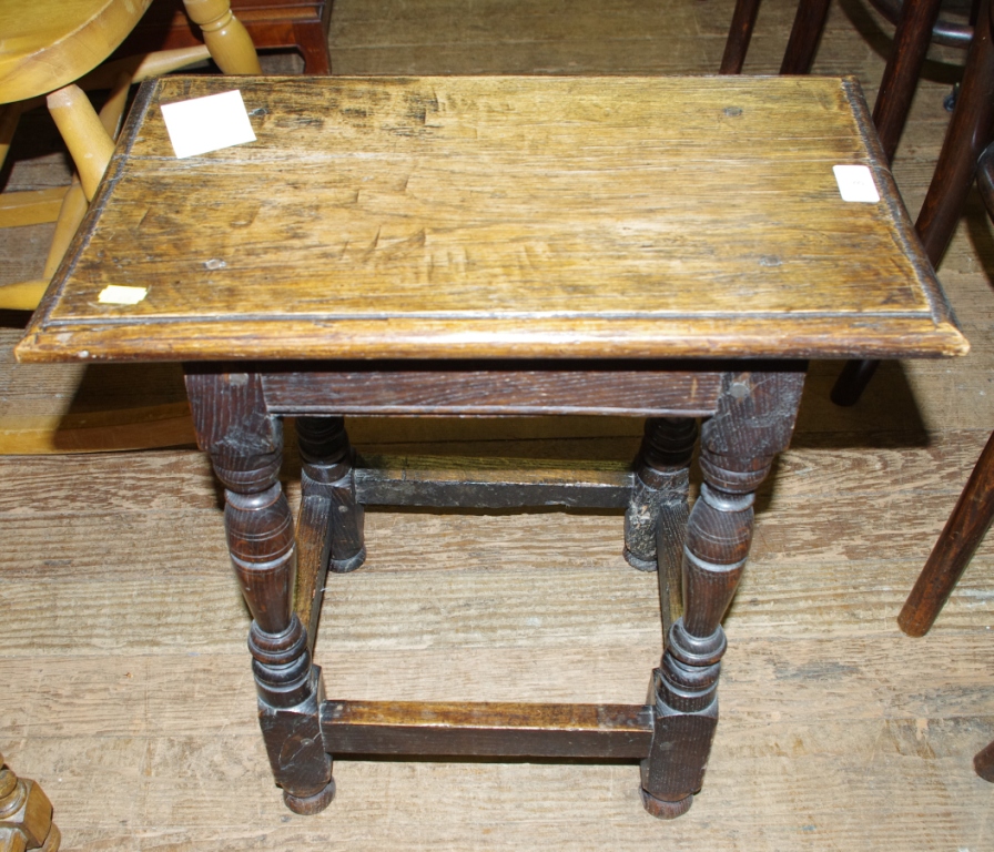 A 19th century oak stained oblong shaped stool raised on turned legs and stretcher support