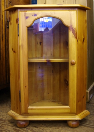 A small pine corner cabinet with glass front door and shelved interior on bun feet