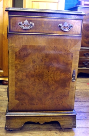 A reproduction walnut and mahogany cross banded bedside cabinet with shaped top, single drawer and