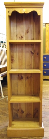 A tall narrow pine bookcase with shaped corners and four shelves under measuring 125x36cm