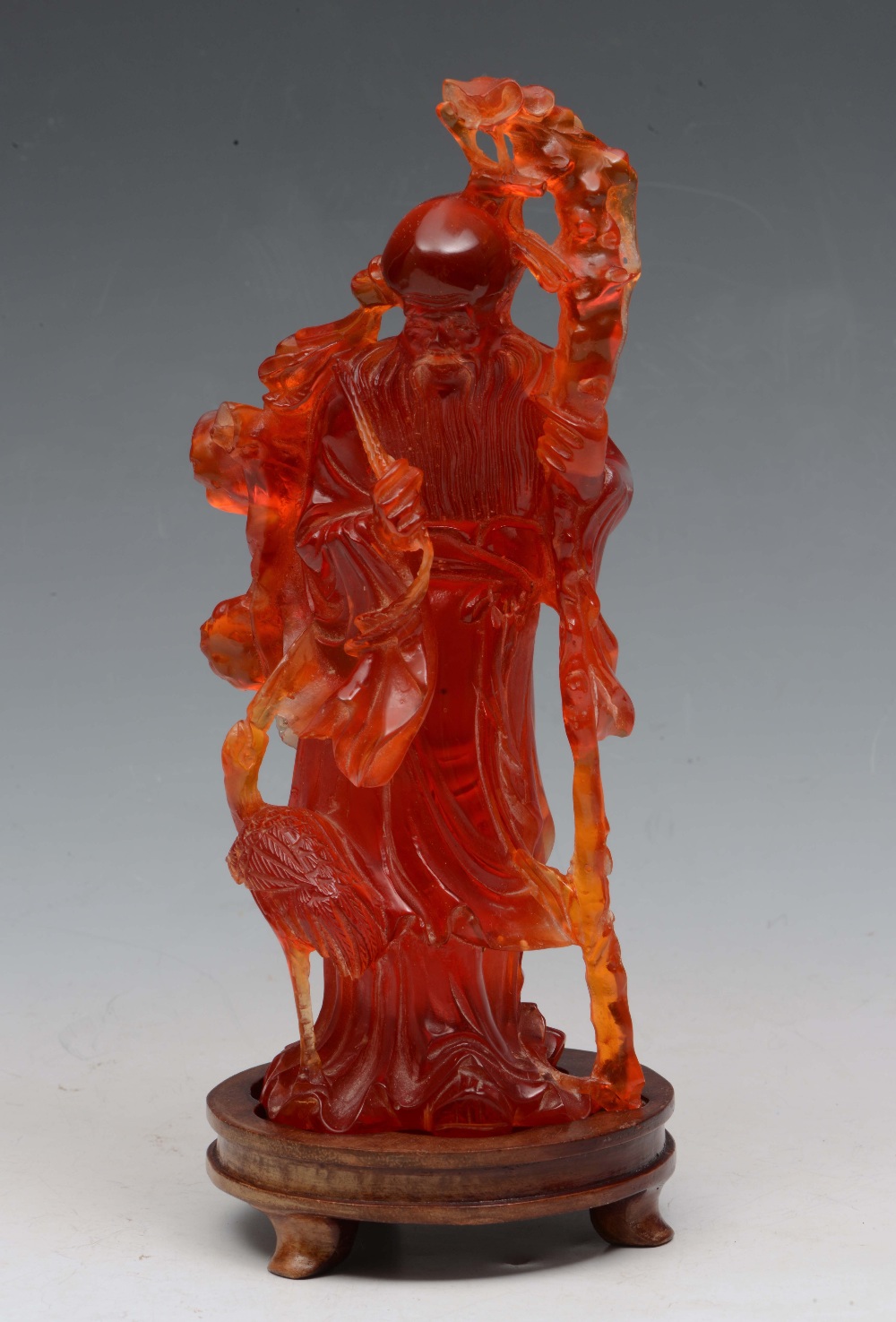 A CHINESE AMBER CARVED MODEL OF LAO TSE holding a staff, on a hardwood circular stand, 19th/20th