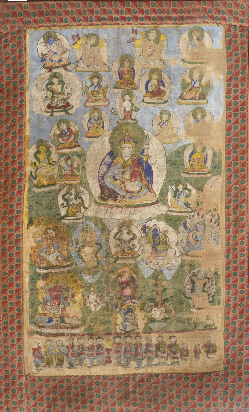 A TIBETAN THANGKA, painted on cloth with a central depiction of Padmasambhava holding a vajra in his