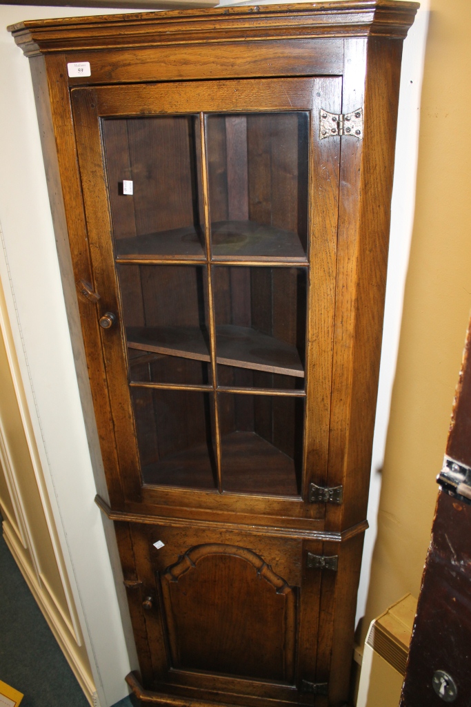 AN OAK REPRODUCTION CORNER CUPBOARD, the interior fitted shelves enclosed by glazed door and