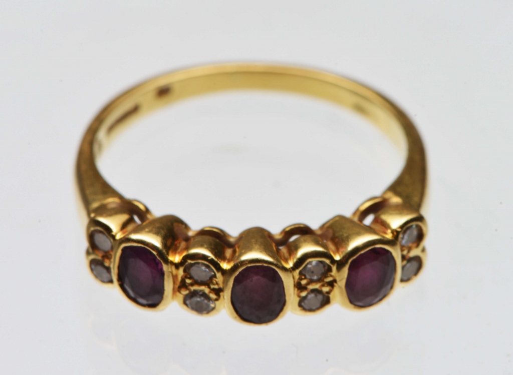 A RUBY AND DIAMOND SET DRESS RING, three oval facet cut rubies mounted in rub over settings with two