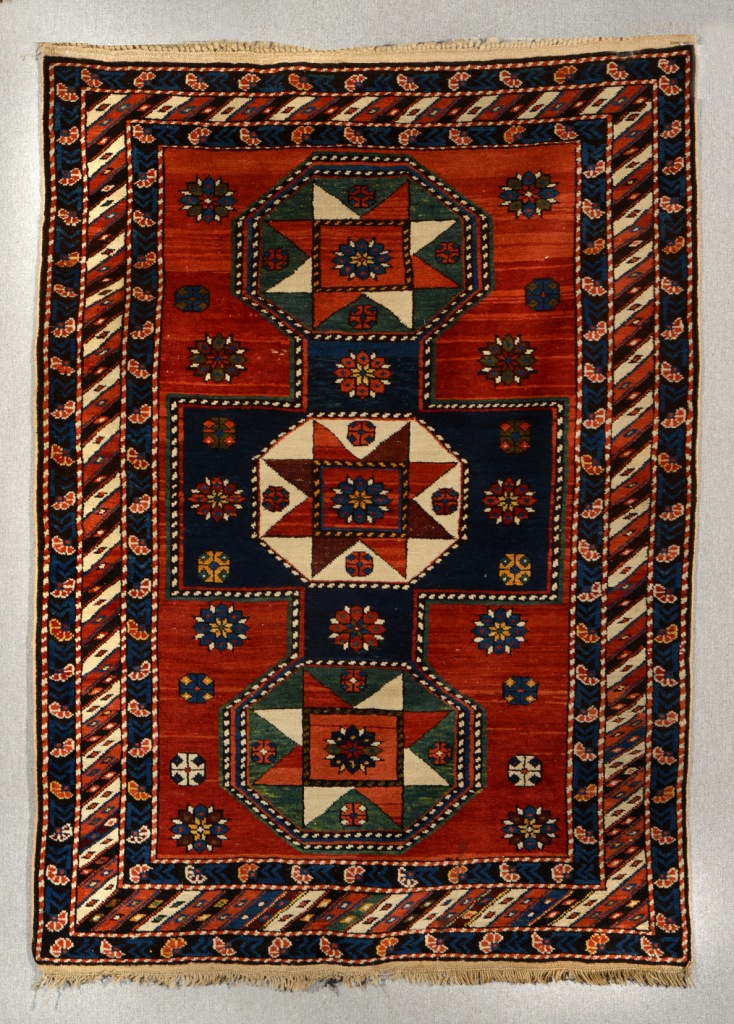 A CAUCASIAN RED GROUND RUG, the central interlinked multiple multicoloured medallion within a