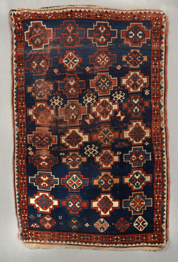 AN ANTIQUE CAUCASIAN BLUE GROUND RUG decorated four rows of nine geometric medallions within a