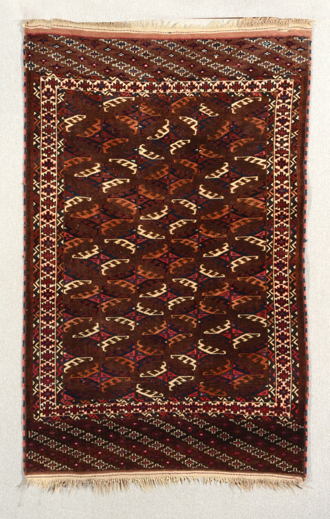 A YOMUT WINE GROUND RUG decorated six rows of hooked rectangular medallions within a geometric