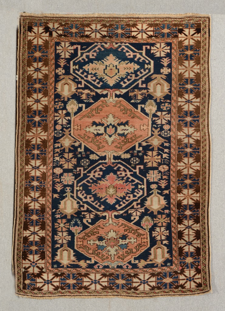 A CAUCASIAN BLUE GROUND MAT decorated four interlinked medallions within a border of stylised