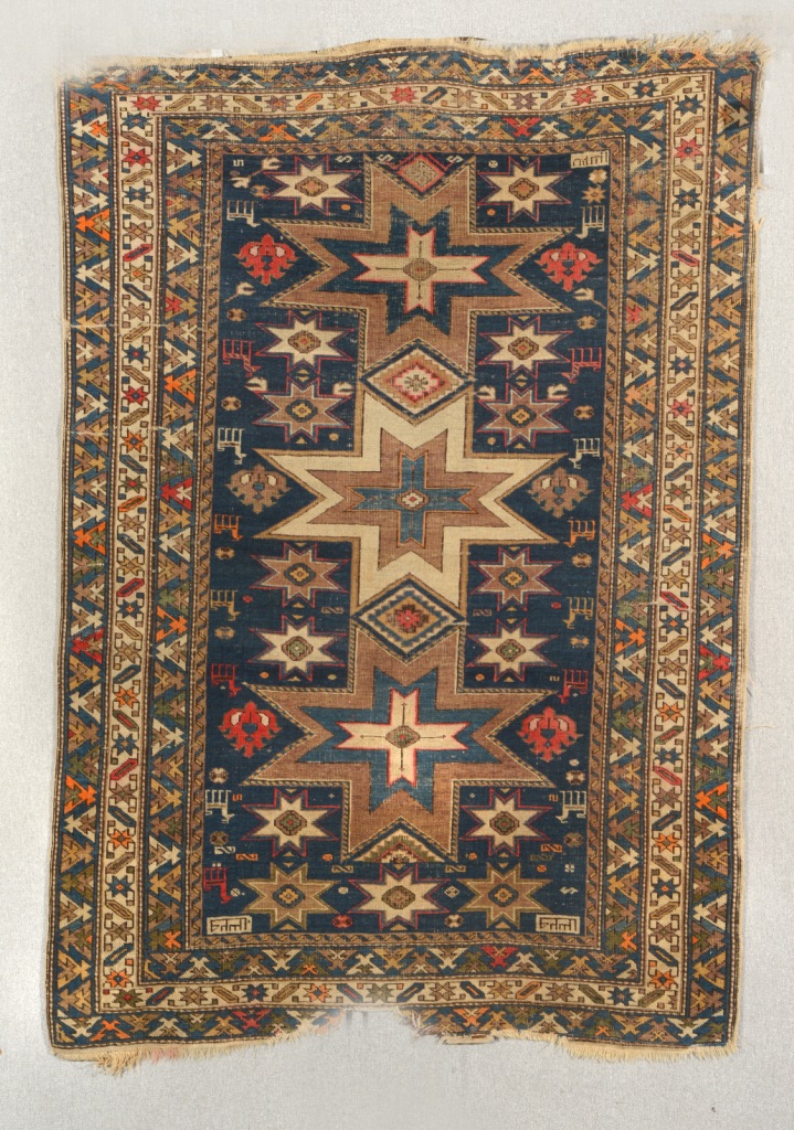 AN OLD CAUCASIAN BLUE GROUND RUG decorated a central multiple star and animal design within a