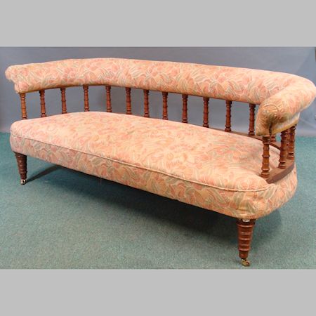 A Victorian oak framed sofa, having a padded top rail and spindle back on turned legs and castors,