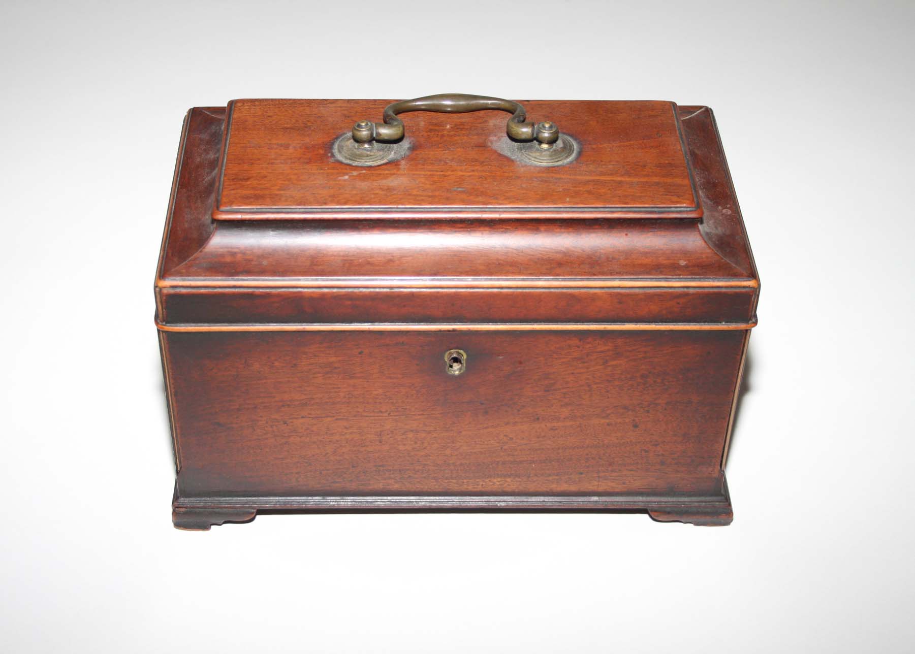 A GEORGE III MAHOGANY TEA CADDY
of sarcophagus form, the hinged top with a brass handle, raised on