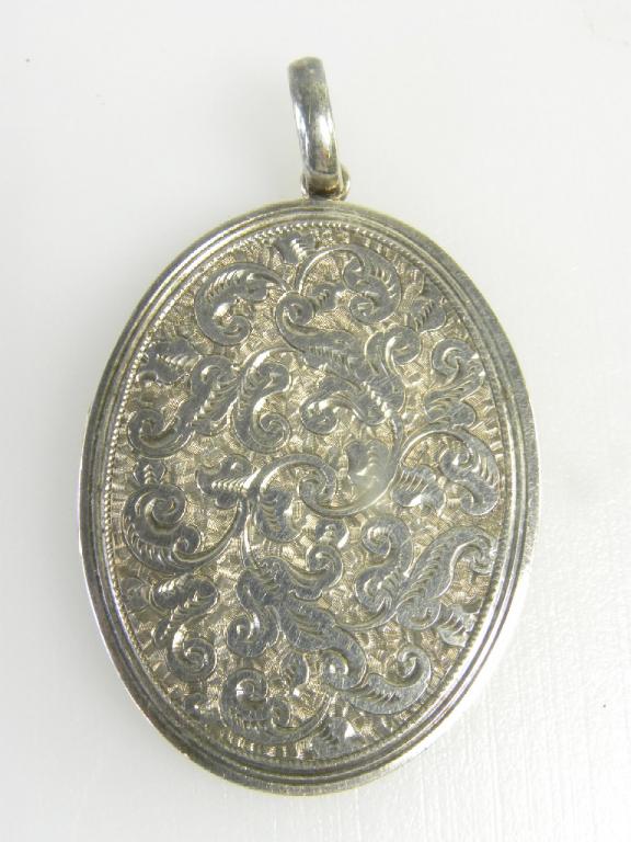 A VICTORIAN SILVER LOCKET WITH ENGRAVED OVAL LID CONTAINING TWO CONTEMPORARY PHOTOGRAPHS