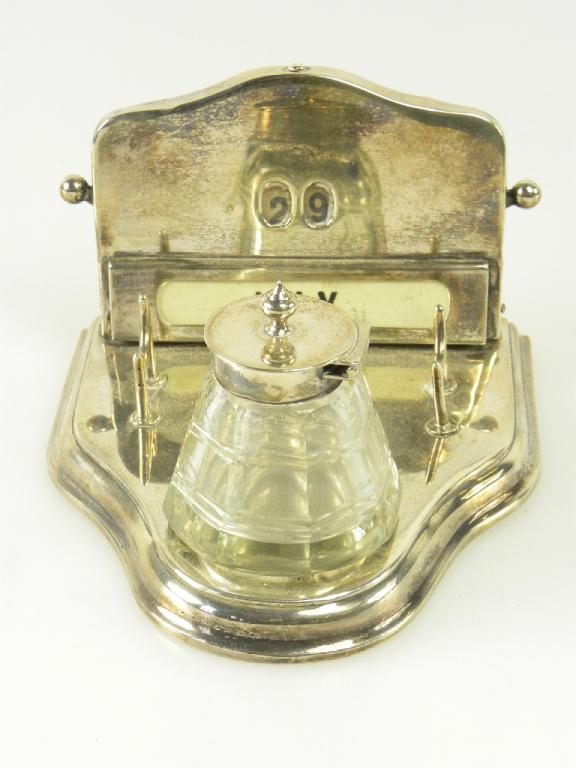 AN EDWARD VII SILVER INKSTAND WITH PERPETUAL CALENDAR, PEN REST AND SILVER MOUNTED FACETED GLASS