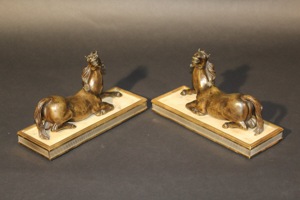 A pair of 19th century French bronze figures of startled recumbent horses on grey veined white