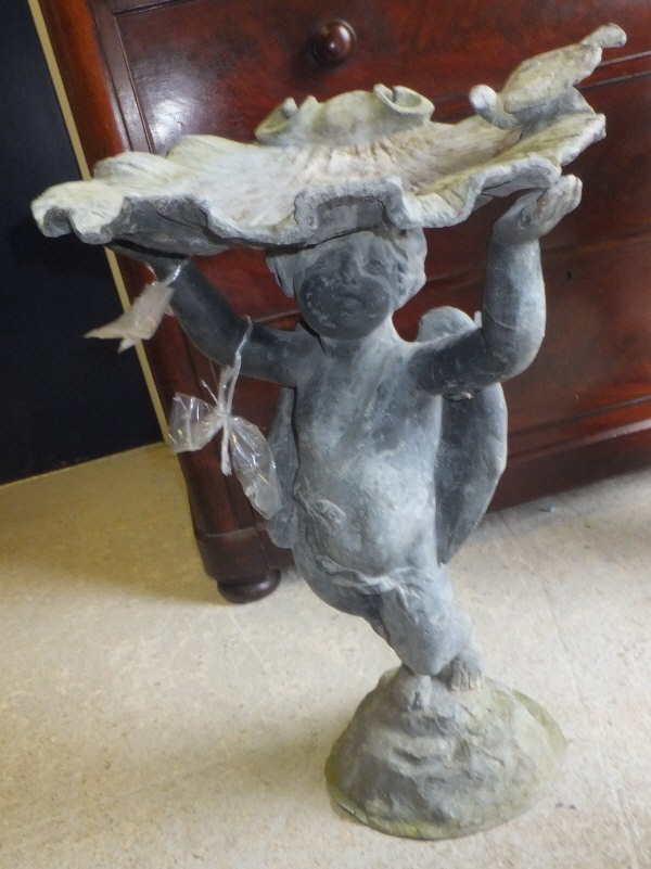 A lead bird bath, the bath in the form of a shell supported by a cherub on a rocky base
