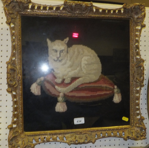 A woolwork needlework panel depicting a seated cat on a coloured cushion on a black ground within