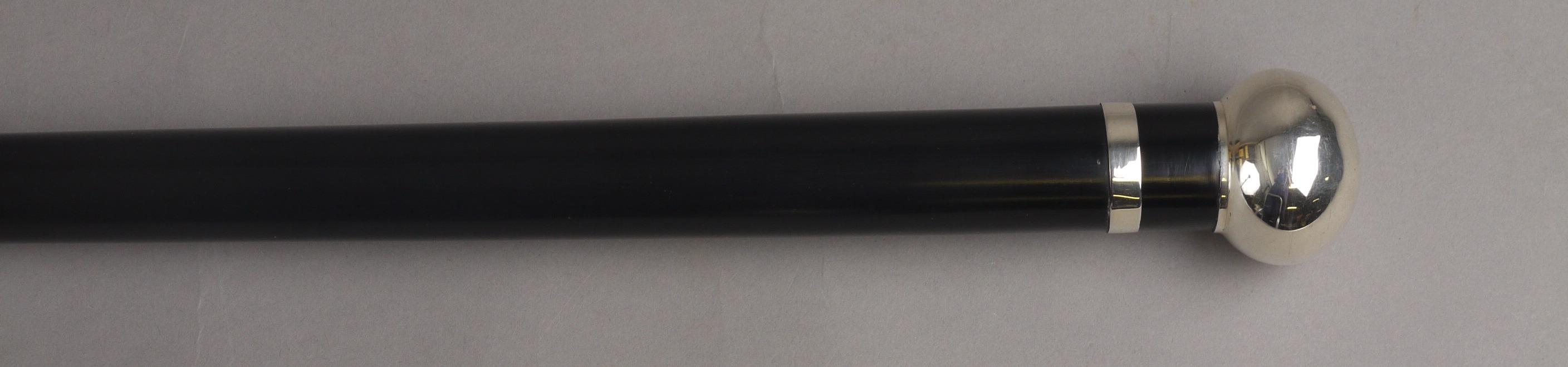 AN EDWARD VII EBONISED WALKING CANE, with tapering stem, silver ball knop and collar, Birmingham,