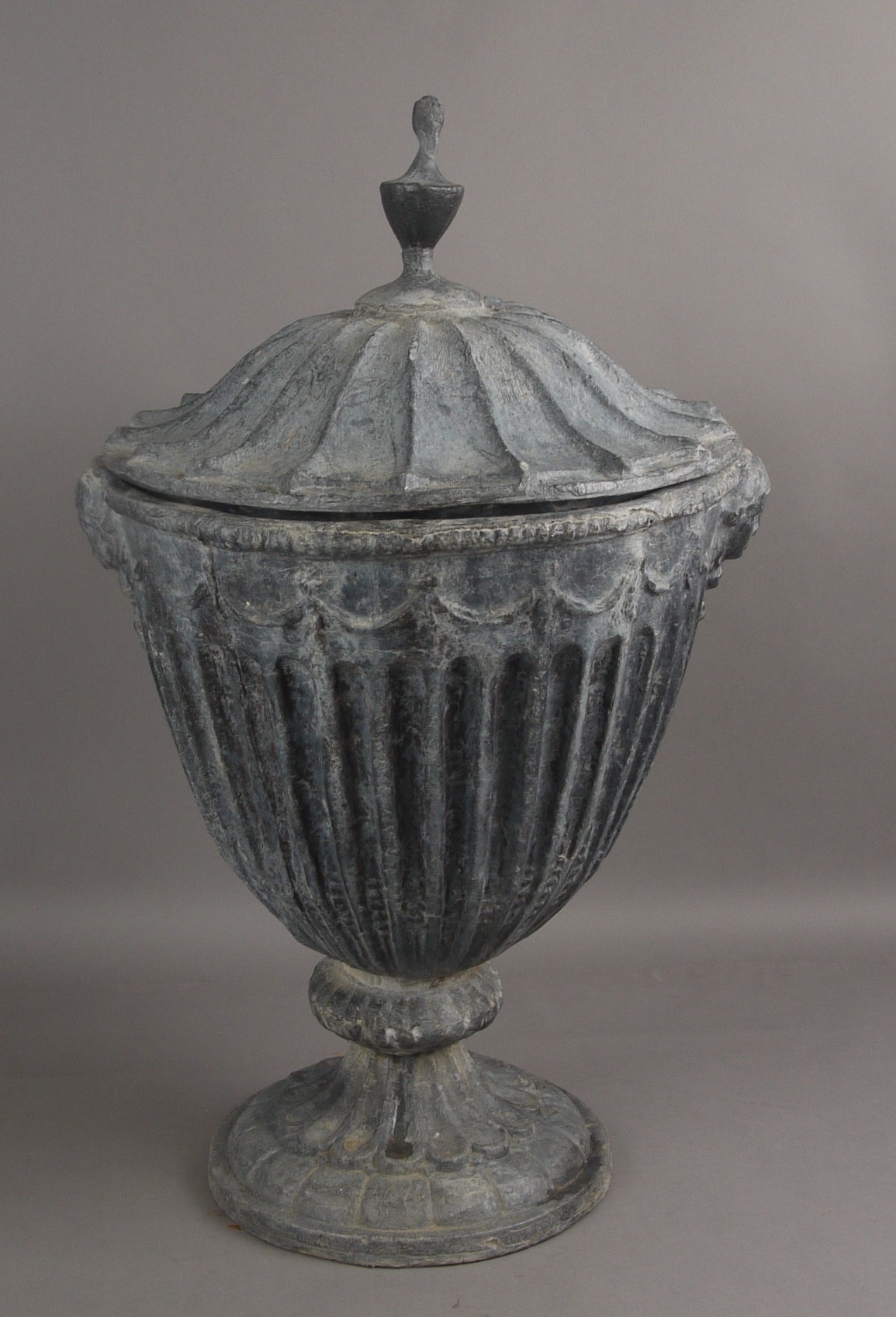 A NEO CLASSICAL STYLE LEAD GARDEN URN AND COVER, of fluted ovoid form, with mask handles, 61cm high