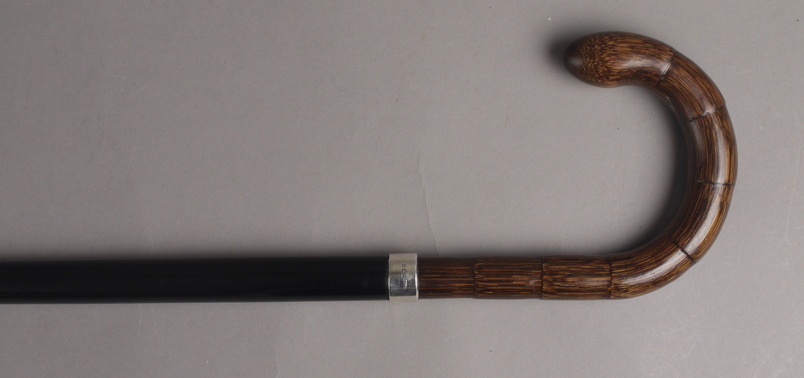 A GEORGE V EBONISED WALKING STICK, with a stained bamboo scroll handle and silver collar, London