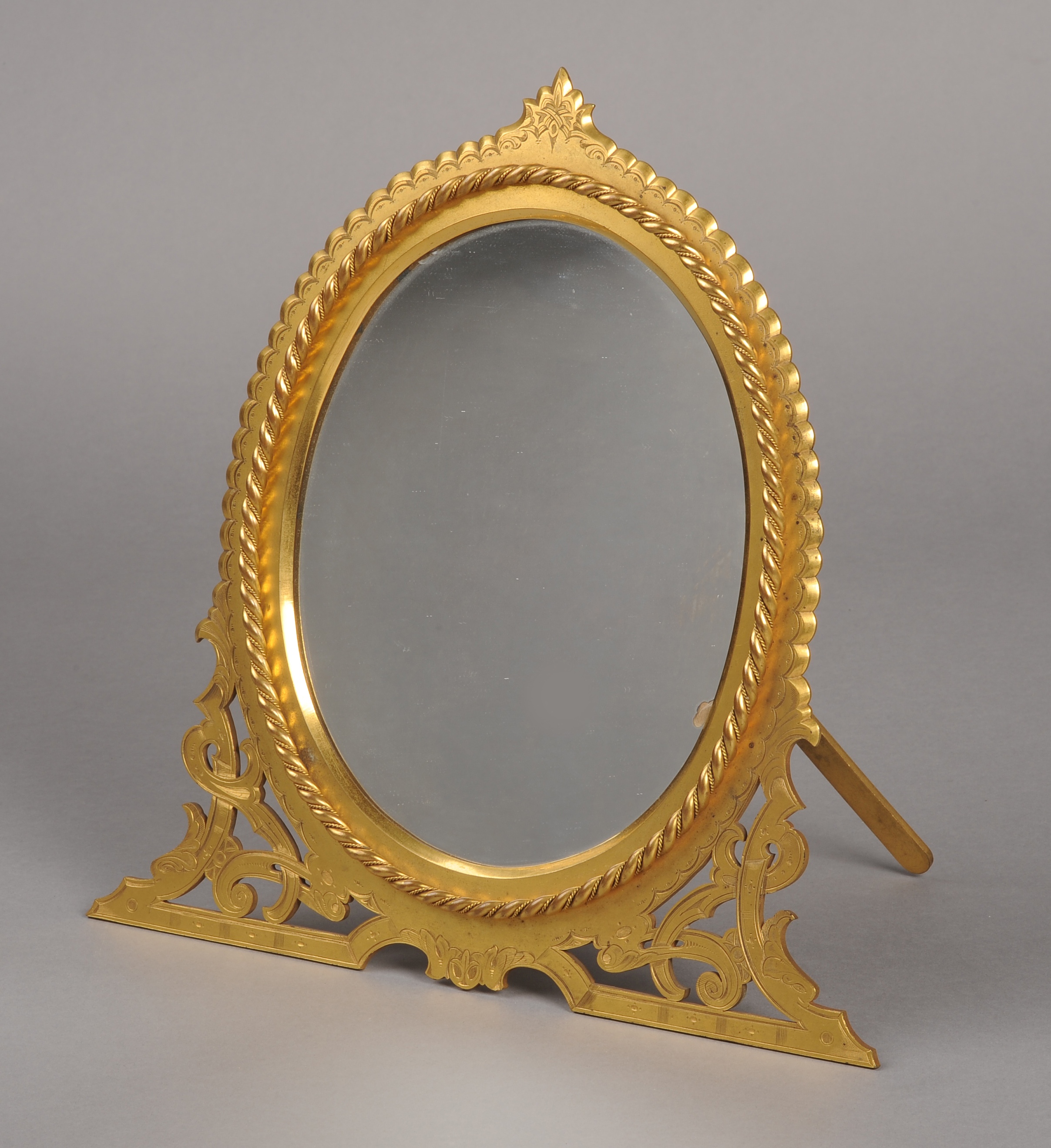 AN EARLY 20TH CENTURY GILT BRASS EASEL MIRROR, oval, the glass within a rope border, pierced