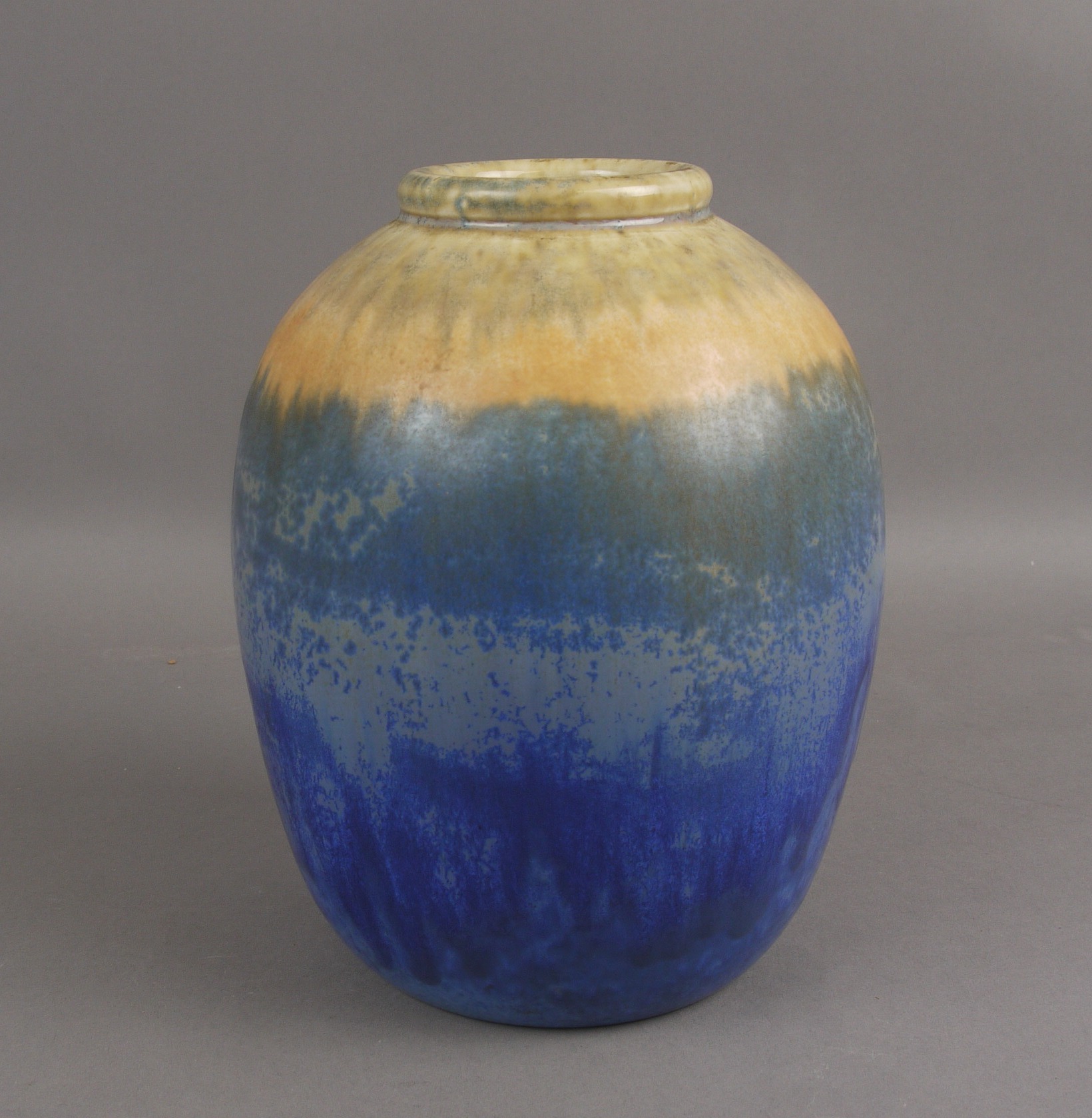 A RUSKIN POTTERY VASE, of squat form with crystalline glaze running from ochre to orange and blue,