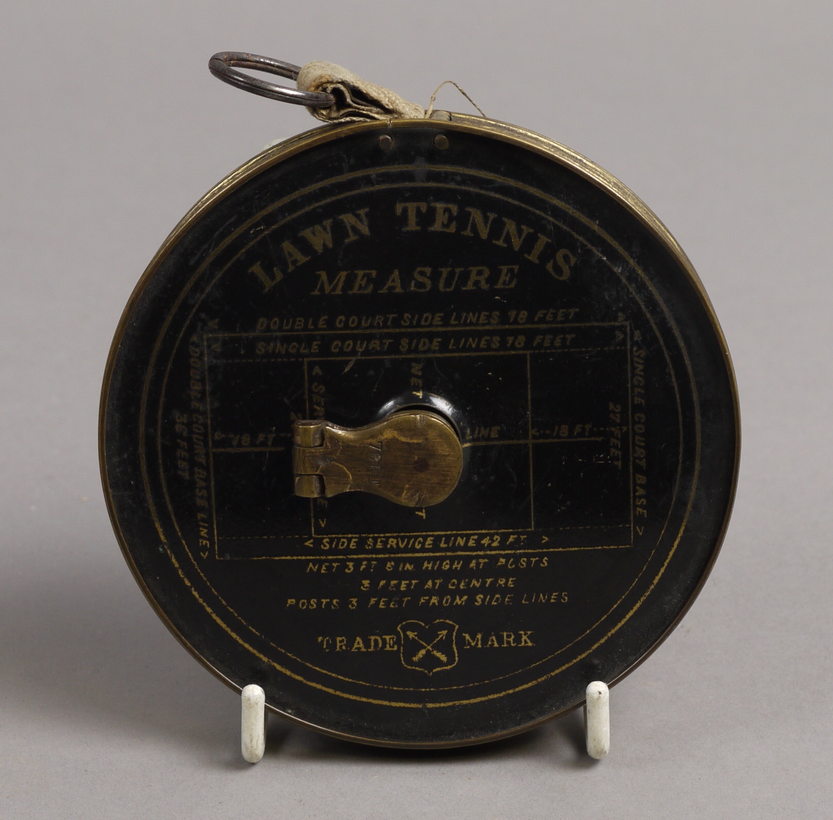 AN EARLY 20TH CENTURY BRASS CASED LAWN TENNIS MEASURE, the face enamelled in black with gilt
