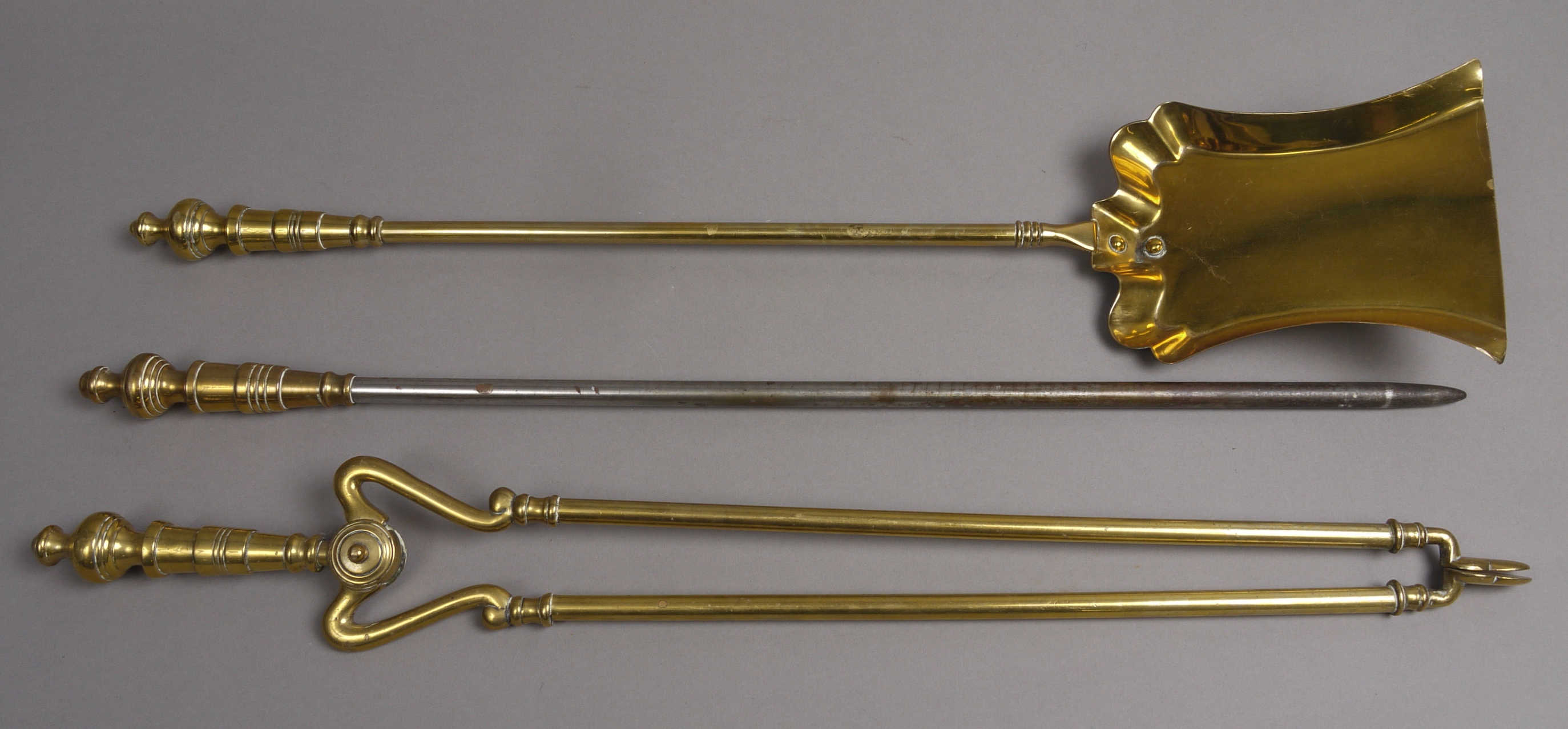 A SET OF THREE VICTORIAN BRASS FIRE IRONS, with urn handles and plain shafts