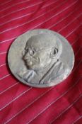 Gandhi a metal medallion bearing an embossed portrait of Gandhi showing him hs looking seriously