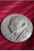 Gandhi a similar lot metal medallion bearing an embossed portrait of Gandhi showing him hs looking