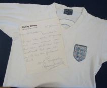 Bobby Moore England Shirt: A white short sleeved v-neck shirt with embroidered 3 Lions England badge