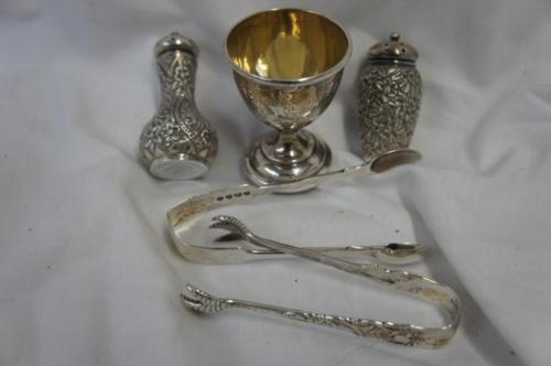 Small collection of silver including two sets of sugar tongs, two chased pepper pots and an egg cup.