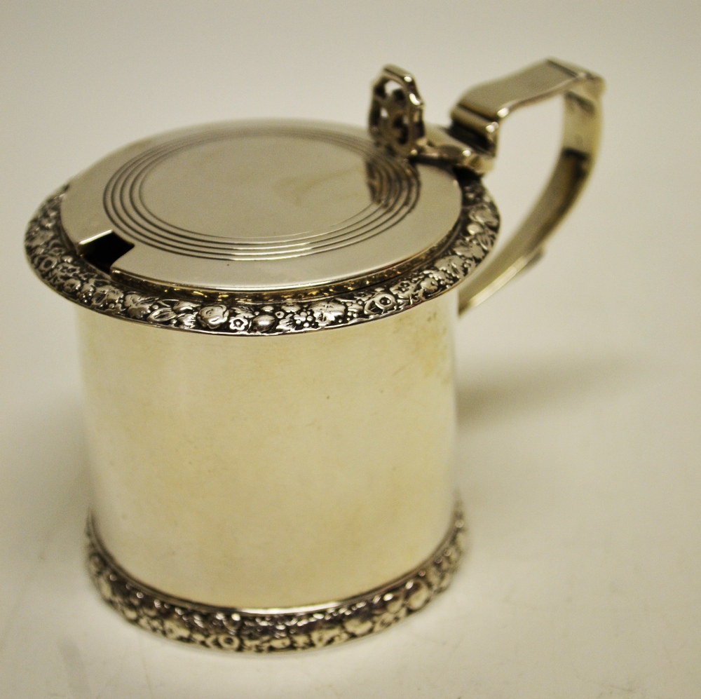 A Victorian silver drum shape mustard pot, with chased borders of flowers, the hinged cover engraved