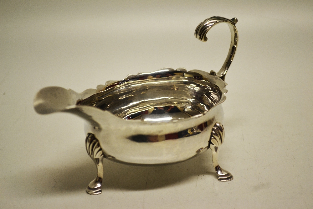 A George III silver oval cream boat, with a fret edge, having a leaf capped scroll handle on shell