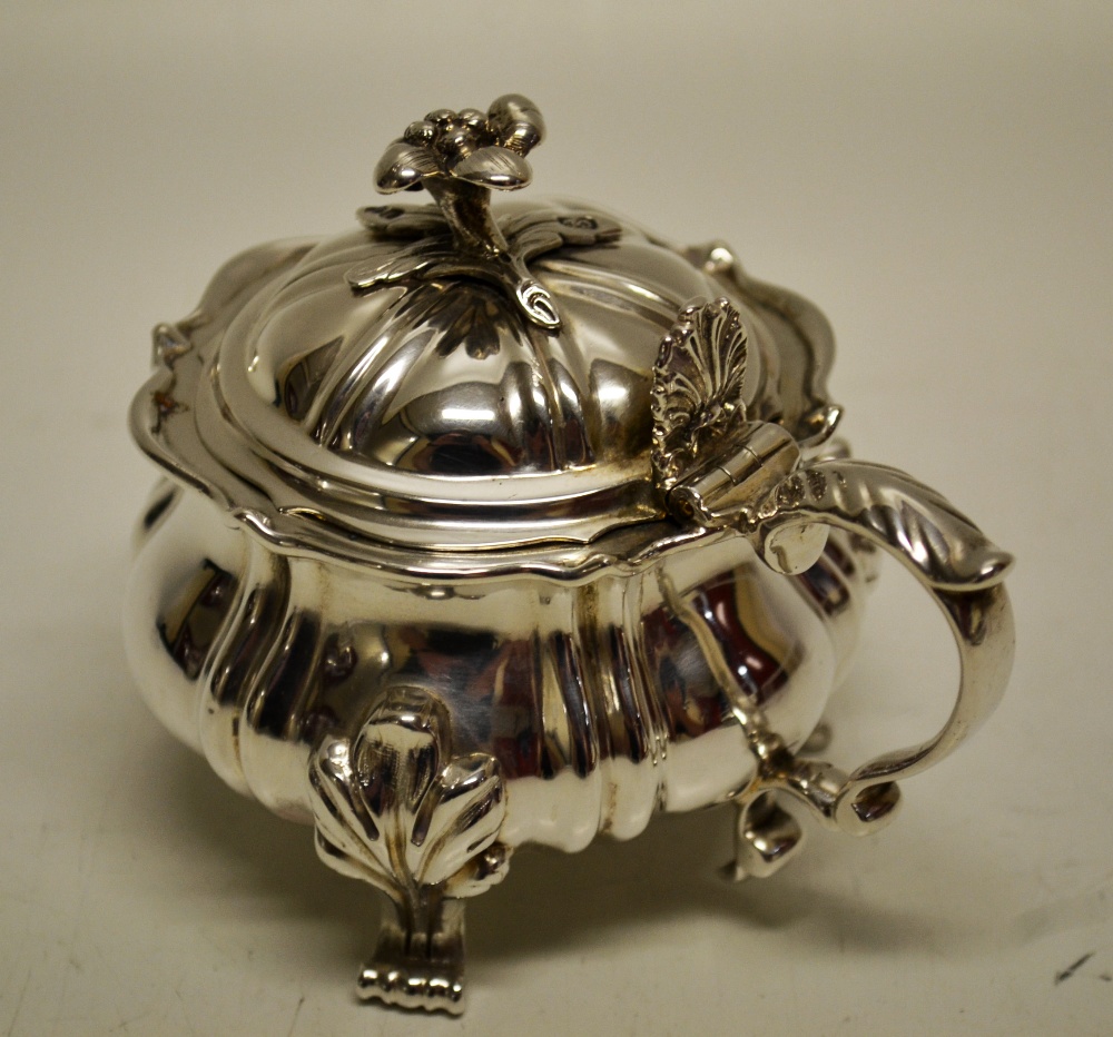 A William IV silver mustard pot, the ogee serpentine sides with ribbing, on a leaf spray cast scroll