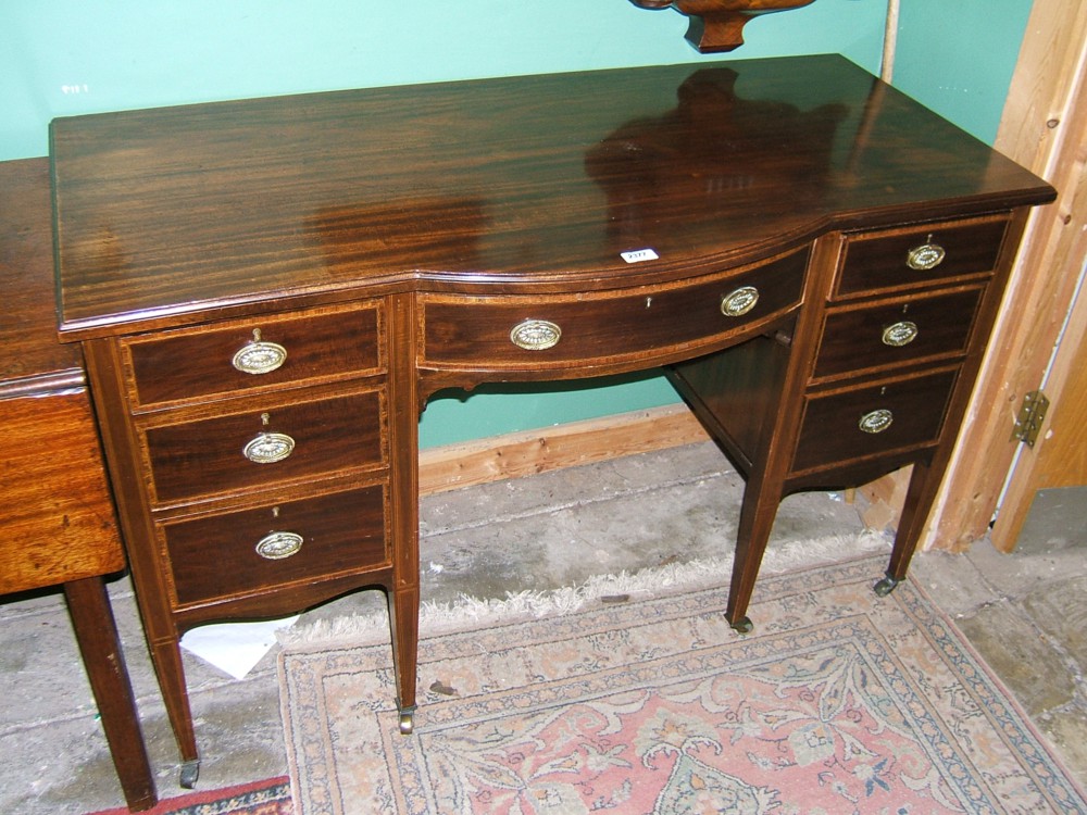 An Edwardian Mahogany Kneehole Desk having plain top with moulded edge, central bow front drawer